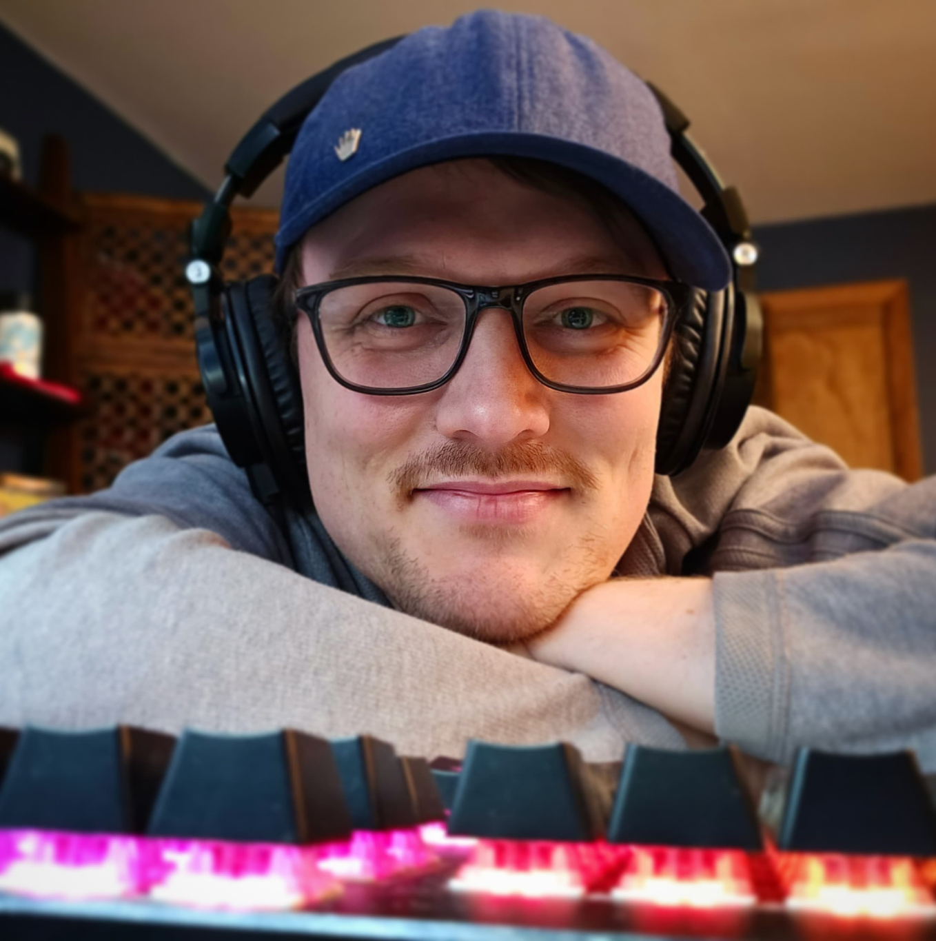 John Lano leaning on desk in front of keyboard with studio headphones on and glasses on face